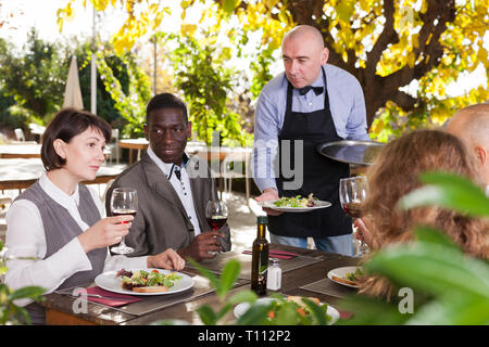 Cameriere che serve pasti al cordiale compagnia presso il ristorante all'aperto Foto Stock