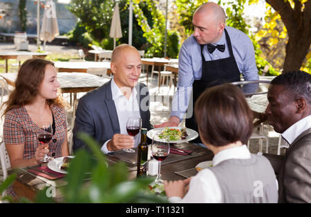 Cameriere che serve pasti al cordiale compagnia presso il ristorante all'aperto Foto Stock