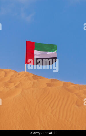 Bandiera degli Emirati arabi uniti al vento sulla cima di un arancio duna di sabbia nel cielo blu a Ras al Khaimah Emirati Arabi Uniti. Foto Stock