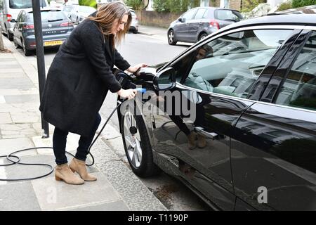 Donna collegando in jaguar elettrico sulla strada residenziale Foto Stock