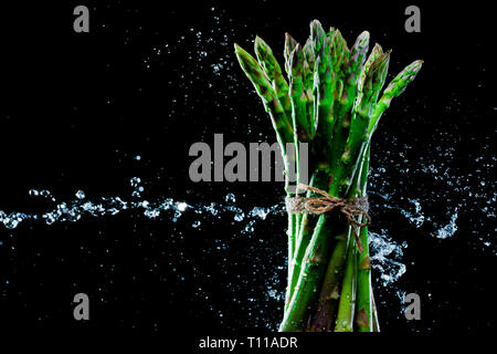 Asparagi in schizzi su sfondo nero. Close-up. Una serie di frutta e verdura in movimento. Foto Stock