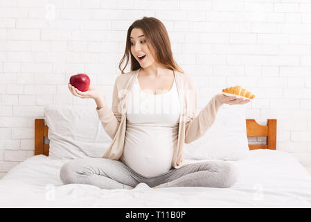 Donna incinta scegliendo tra un croissant e Apple Foto Stock