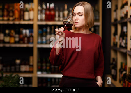 Immagine della bionda con vetro in mani al negozio con il vino Foto Stock