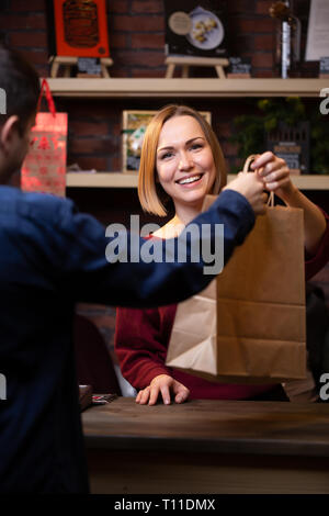 Foto di felice venditore bionda dando sacchetto di carta per uomo Foto Stock