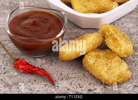 Pepite di pollo con peperoncino rosso e salsa barbecue su un sfondo di calcestruzzo. Foto Stock