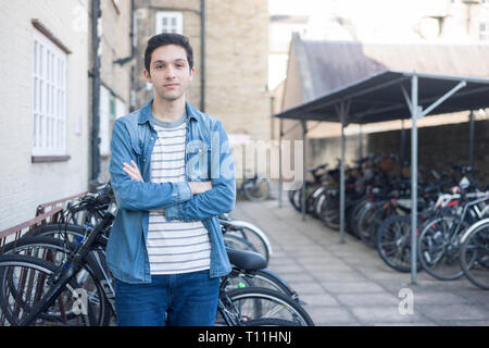 Un giovane uomo si erge tra un carico di biciclette in un deposito bici posizione in un College di Cambridge. Foto Stock