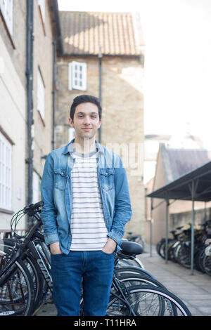 Un giovane uomo si erge tra un carico di biciclette in un deposito bici posizione in un College di Cambridge. Foto Stock