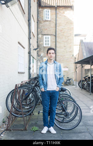 Un giovane uomo si erge tra un carico di biciclette in un deposito bici posizione in un College di Cambridge. Foto Stock