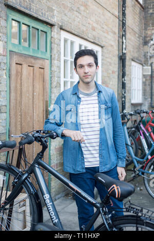 Un giovane uomo si erge tra un carico di biciclette in un deposito bici posizione in un College di Cambridge. Foto Stock