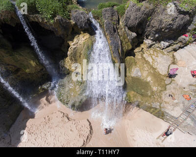 Un uomo prendere un bagno in cascata e usarlo come una doccia. La cascata effettivamente si immerge verso il mare Foto Stock