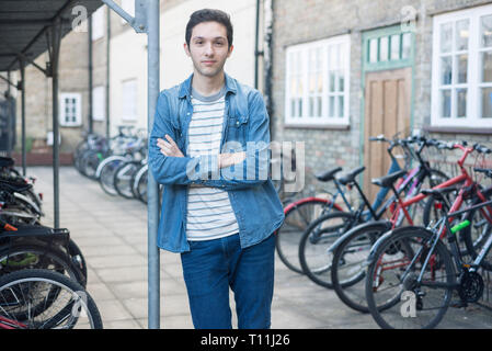 Un giovane uomo si erge tra un carico di biciclette in un deposito bici posizione in un College di Cambridge. Foto Stock