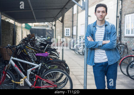 Un giovane uomo si erge tra un carico di biciclette in un deposito bici posizione in un College di Cambridge. Foto Stock