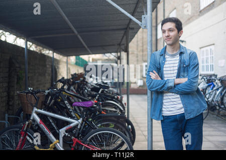 Un giovane uomo si erge tra un carico di biciclette in un deposito bici posizione in un College di Cambridge. Foto Stock