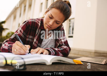 Donna seduta dello studente al college campus e rendere note. Una studentessa studiare all università campus. Foto Stock