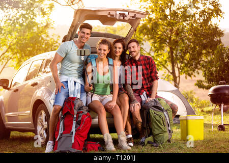 Felice popolo sorridente sul viaggio di campeggio nel tronco rendere selfie durante il disimballaggio Foto Stock