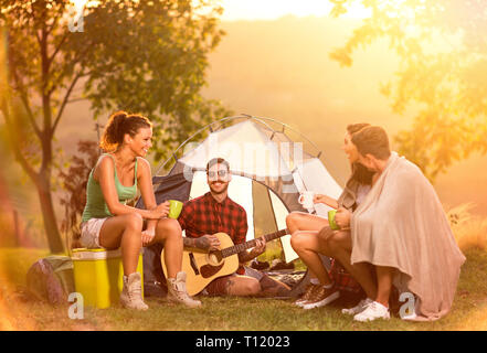 Gruppo di camper prossima tenda divertirsi a suonare la chitarra e cantare Foto Stock