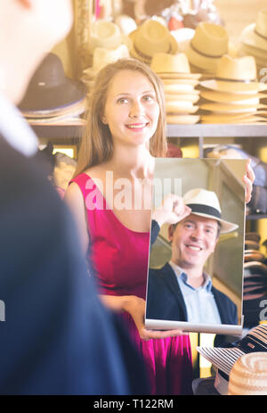 Felice femmina specchio di contenimento e mostrando il suo maschio della riflessione in cappelli shopping mall Foto Stock