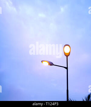 Luci di strada che brillano di luce nella sera e isolate contro il cielo blu crepuscolo. Foto Stock