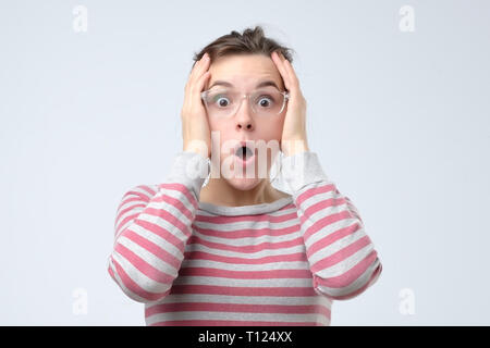 Lo stress e il concetto di shock. Giovane donna sorpresa stringendo la testa nelle mani. Negativo emozione per il viso Foto Stock