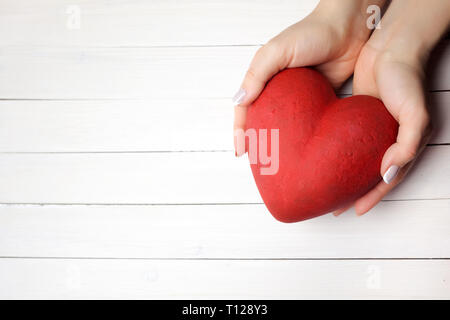 Donna che mantiene le mani cuore rosso su bianco sullo sfondo di legno, vista dall'alto Foto Stock