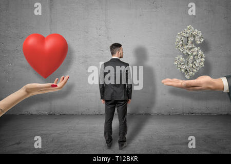 Imprenditore in piedi tra mano azienda cuore rosso e la mano che regge il denaro del dollaro sul muro grigio sfondo Foto Stock