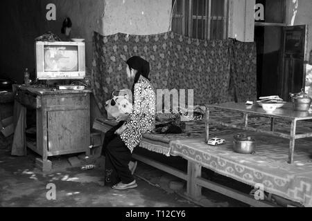 Giovane donna uighur che guarda la tv, villaggio di Tuyuq, regione autonoma di Xinjiang, Cina. Foto Stock