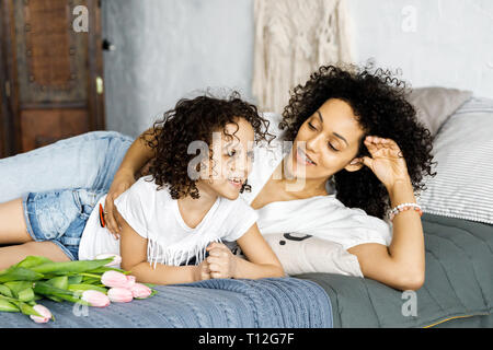 Mom e poco carino curly ragazza seduta sul letto con i tulipani nelle loro mani. Foto Stock