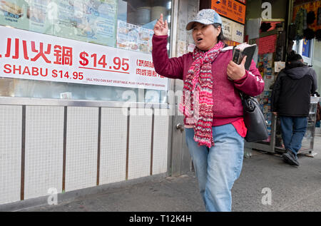 Un religioso donna cinese tenendo una bibbia passeggiate sulla via principale di Chinatown di recitare passaggi e cercando di coinvolgere gli sconosciuti. In lavaggio, Queens, NYC Foto Stock