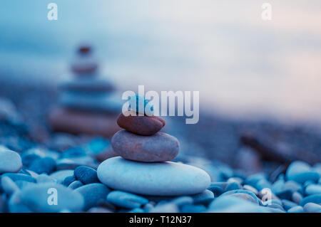 Piramide piegata Zen pietre ghiaia sul mare spiaggia al tramonto Foto Stock