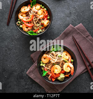 Stir fry con la sua pasta di soba, gamberi (gamberetti) e verdure. Asian cibo sano, mescolare farina fritto in un recipiente su sfondo nero, copia dello spazio. Foto Stock
