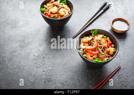 Stir fry con la sua pasta di soba, gamberi (gamberetti) e verdure. Asian cibo sano, mescolare farina fritto in un recipiente su sfondo nero, copia dello spazio. Foto Stock