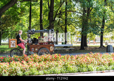 Varsavia, Polonia - Agosto 23, 2018: giovane uomo bicicletta equitazione Bicicletta cioccolata calda fast food stand coffee shop in estate Giardini Saxon Park Foto Stock