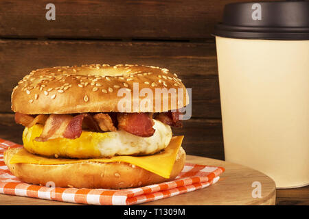 La prima colazione a sandwich con asse di legno in background. Bagel, l'uovo, il formaggio e la pancetta. Foto Stock