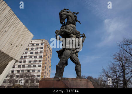 Il Palazzo dello Sport di edificio con la leggenda del guerriero Kojomkul scultura di fronte. Il palazzo è un esempio di comunista sovietico brutalist architettura Foto Stock