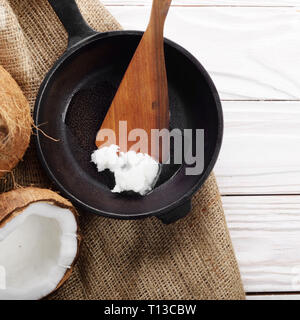 Noce di cocco, shell con carne, padella in ghisa e la spatola sulla canapa sacco su legno bianco tavolo da cucina Foto Stock