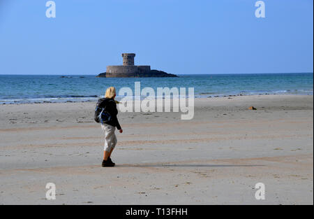 La donna gli escursionisti a piedi sulla spiaggia nei pressi de La Torre Rocco su un isola di marea in St Ouen's Bay sull'isola di Jersey, nelle Isole del Canale, UK. Foto Stock