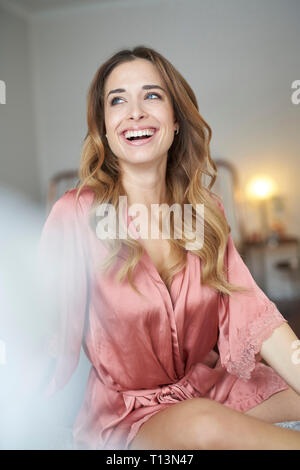 Felice giovane donna in vestaglia seduta sul letto Foto Stock