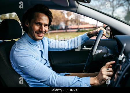 Ritratto di imprenditore sorridente auto pilotaggio tramite telefono cellulare come sistema di navigazione Foto Stock