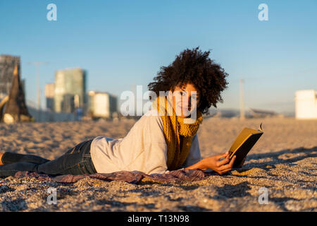 La donna che giace nella sabbia, relax sulla spiaggia, la lettura di un libro Foto Stock