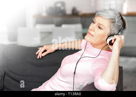 Ritratto di donna matura seduti sul divano ascoltando musica con le cuffie Foto Stock