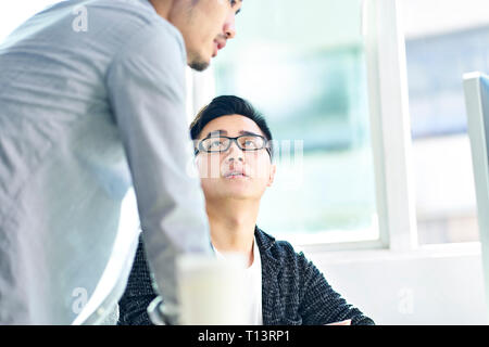 Due giovani imprenditori asiatici avente una discussione nella parte anteriore del computer in ufficio. Foto Stock