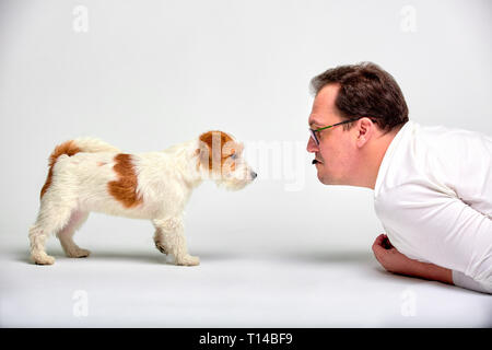 Ritratto di uomo felice sdraiato sul pavimento, giocando con gli adorabili Jack Russell Terrier Il cucciolo di vuoti interni studio su sfondo bianco. Il pet lover concept Foto Stock