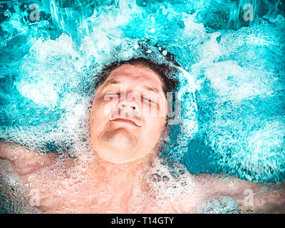 Uomo felice rilassarsi nella jacuzzi e chiudendo gli occhi. Ragazzo caucasico di riposo in un pool consiste nell'acqua. Vista da sopra. Ragazzo di nuoto in piscina con Foto Stock