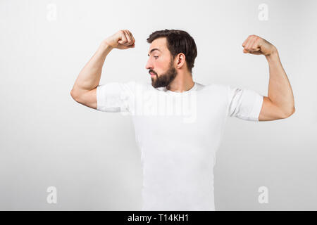 Un bel fiducioso giovane uomo in piedi e mostrando grandi muscoli nelle sue mani. Egli è alla ricerca di uno di loro e molto orgogliosa di loro. Egli indossa una whi Foto Stock