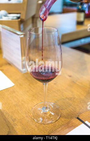Degustazione di vino e di vino rosso che viene versato in un bicchiere di vino su un contatore a un vino station wagon o cantina con messa a fuoco selettiva su bolle nel vetro Foto Stock
