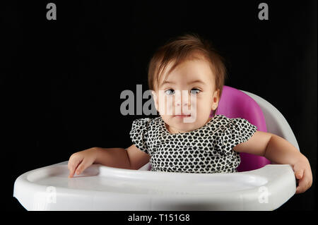 Baby girl sedere sulla sedia a mangiare tabella isolati su sfondo nero Foto Stock