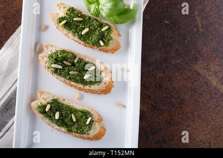 Bruschetta con pesto di basilico sauace e pinoli, su una piastra bianca. Cibo sano, la dieta e il concetto di cucina a vista. Specialità della cucina italiana. Sof selettiva Foto Stock