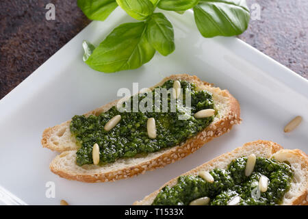 Bruschetta con pesto di basilico sauace e pinoli, su una piastra bianca. Cibo sano, la dieta e il concetto di cucina a vista. Specialità della cucina italiana. Sof selettiva Foto Stock