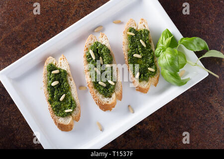 Bruschetta con pesto di basilico sauace e pinoli, su una piastra bianca. Cibo sano, la dieta e il concetto di cucina a vista. Specialità della cucina italiana. Sof selettiva Foto Stock