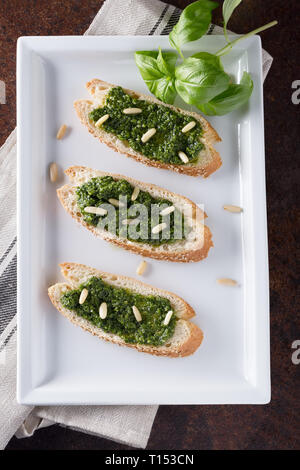 Bruschetta con pesto di basilico sauace e pinoli, su una piastra bianca. Cibo sano, la dieta e il concetto di cucina a vista. Specialità della cucina italiana. Sof selettiva Foto Stock